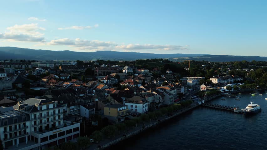 Aerial view of the serene Lake Geneva, with buildings lining the waterfront, contrasting with the dark water and the mountains, Lake Geneva, Nyon, Vaud, Switzerland.