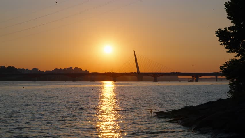 Scenic sunset over the Han River viewed from Hangang Park in Seoul, with Seongsan Bridge silhouetted against the glowing sky and water reflections.