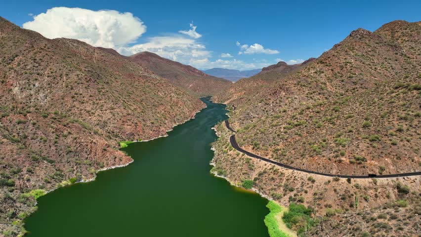 Aerial view of the green Theodore Roosevelt lake winding through arid mountains under a blue sky with sparse clouds, Theodore Roosevelt, Arizona, United States.