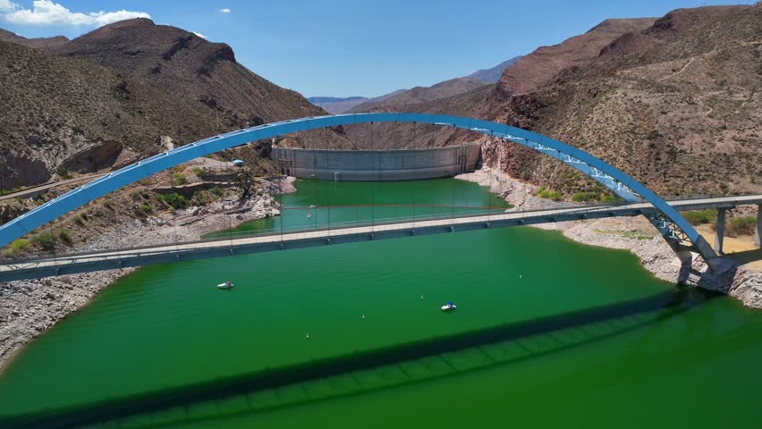Aerial view of the bridge over the vibrant green Theodore Roosevelt Lake, contrasting with the arid, mountainous terrain, Theodore Roosevelt, Arizona, United States.