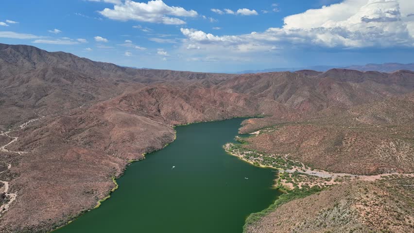 Aerial view of Theodore Roosevelt Lake with its vivid green waters nestled amid the rugged, textured, brown mountains under a blue sky, Theodore Roosevelt, Arizona, United States.