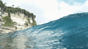 Tropical barrel wave breaking close to rocky island shoreline under blue sky, low frontal view slow motion - Powered by Shutterstock - Get 15% off with code: PIKWIZARD15