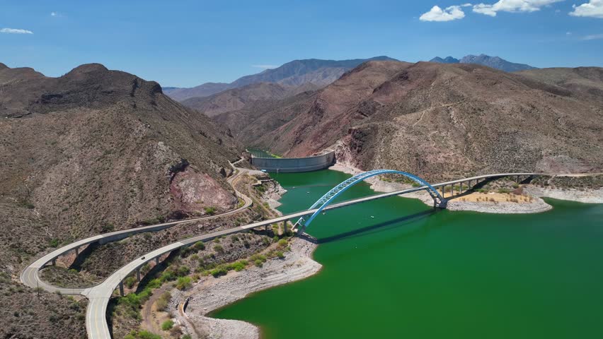 Aerial view of Theodore Roosevelt dam, a concrete arch dam on the Salt River, with bridge and green water contrasting the arid landscape, Theodore Roosevelt lake, Arizona, United States.