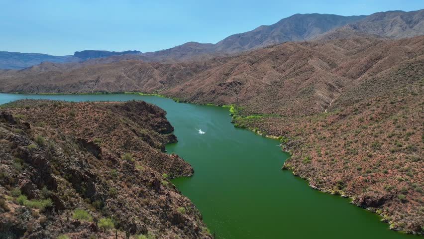Aerial view of the Theodore Roosevelt lake with a boat in the green water, surrounded by the brown mountains, Theodore Roosevelt, Arizona, United States.