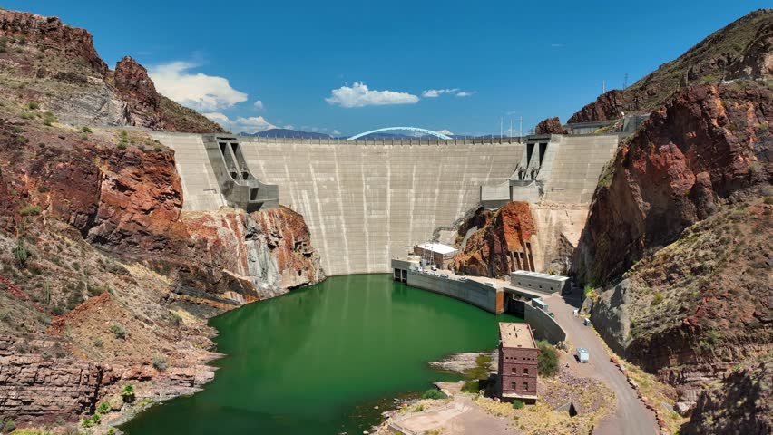 Aerial view of Roosevelt Dam, its concrete structure contrasting with the rugged red rock mountains and the emerald green waters, Theodore Roosevelt lake, Arizona, United States.