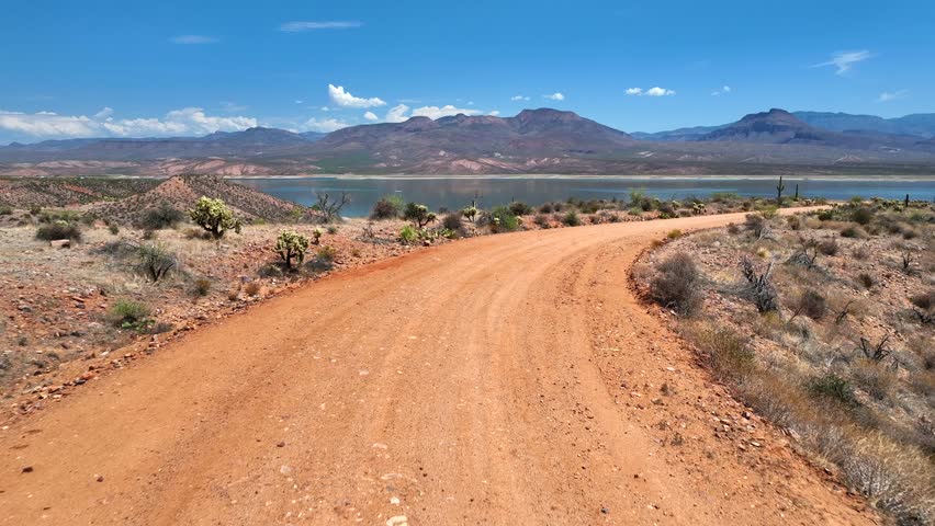 Aerial view of a dirt road leading toward the Theodore Roosevelt lake against a backdrop of distant mountains and clear skies, Theodore Roosevelt, Arizona, United States.