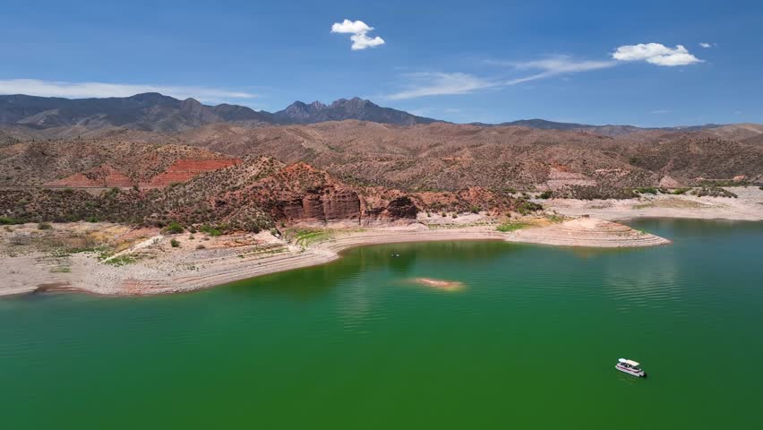 Aerial view of the vividly green Theodore Roosevelt lake surrounded by arid, rocky terrain under a clear blue sky, Theodore Roosevelt lake, Arizona, United States.