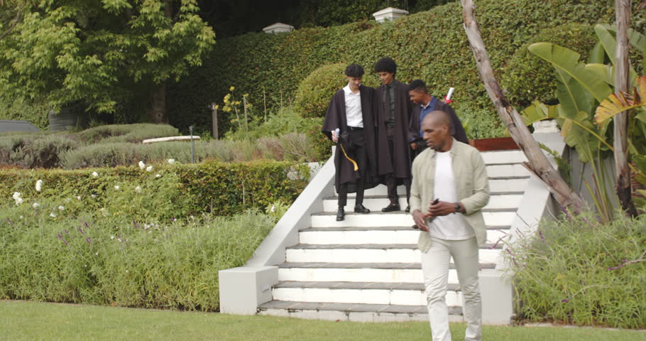 Proud father capturing graduation moment of happy diverse students on garden steps. celebration, achievement, education, diverse family, joy, in backyard