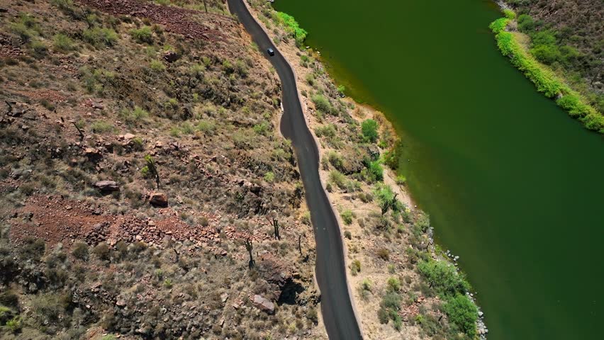 Aerial view of the Theodore Roosevelt lake with its green waters contrasting the rocky mountains and a road running alongside it, Theodore Roosevelt, Arizona, United States.