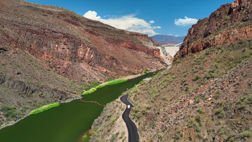 Aerial view of Theodore Roosevelt Dam and lake. The dam is surrounded by rugged, reddish-brown mountains and a winding road, Theodore Roosevelt lake, Arizona, United States.