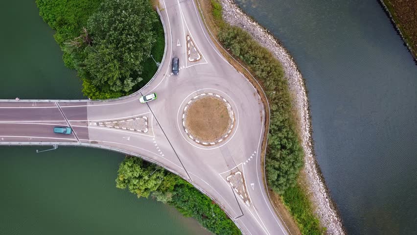 Aerial drone view of roundabout surrounded by water canals and greenery in Marina di Ravenna, Italy, scenic traffic flow and road patterns from above.