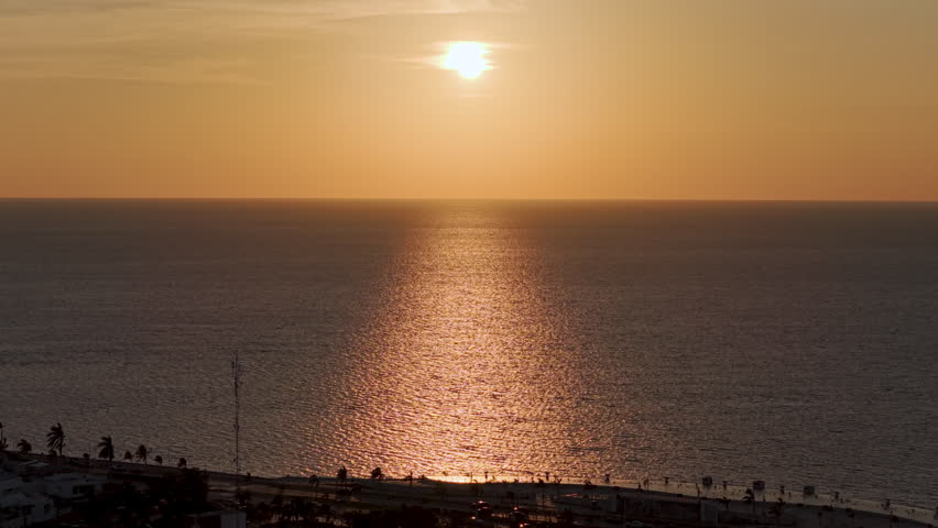 Aerial view of the sun setting over the Gulf of Mexico, casting golden reflections on the water near the waterfront promenade in Campeche, Mexico.