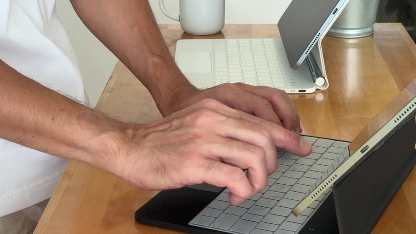 person typing on tablet keyboard with laptop in the background, showcasing modern workspace technology.