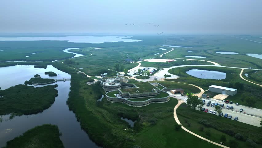 Hazy summer aerial descends and circles eco centre amid sprawling wetlands