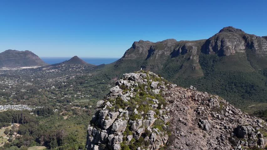 Aerial panoramic view of Cape Town, South Africa, with the Atlantic Ocean in the background, mountain peaks, and a valley below covered in lush green forest