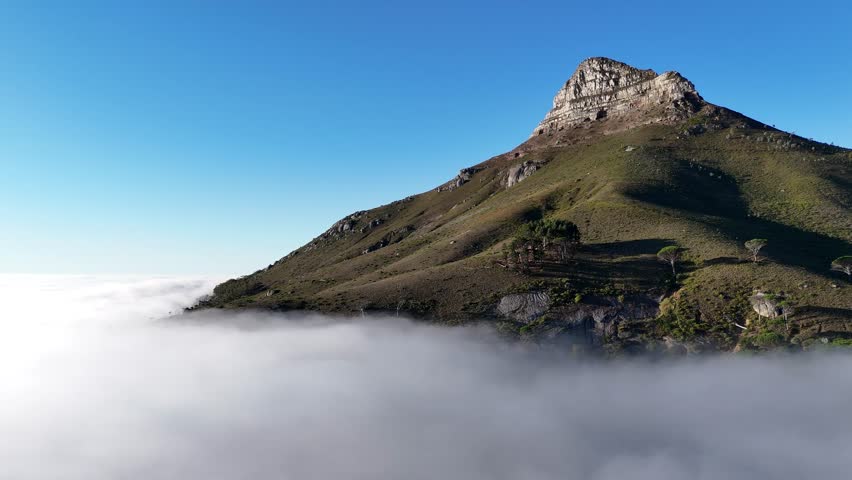 Aerial drone footage of Lion’s Head mountain in Cape Town, South Africa, surrounded by mist and clouds with only the peak emerging above the fog cinematic high angle view of iconic landscape