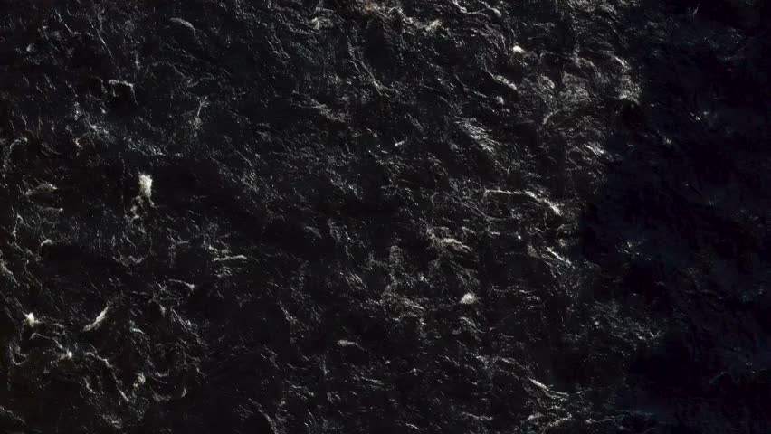 Top down view of black fast flowing water making white foamy waves.