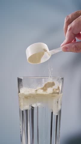 protein powder spills in glass of water from measure scoop.  whey sports nutrition. dry mixture for preparation of sporting or dietary drink.