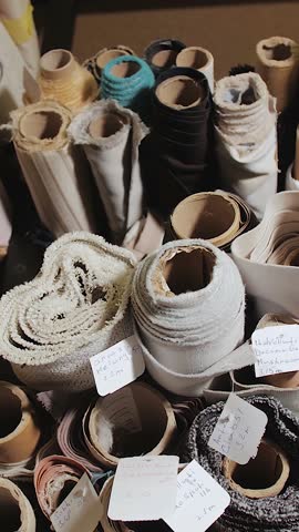 Rolls of fabric and textiles lie in a warehouse of furniture sewing equipment, stacked on shelves of a furniture factory. Close-up of the warehouse, various fabrics. Vertical video.