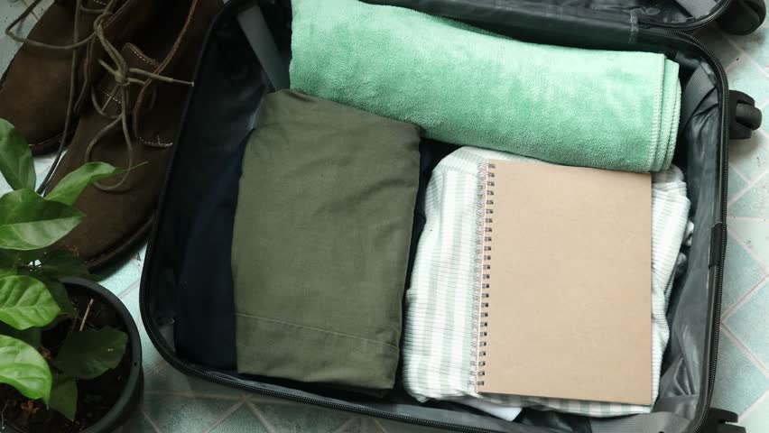 Close up of an unrecognized person getting ready for travel and packing clothes into an open black suitcase, vacation travel concept. Person preparing for a trip and folding clothes into a luggage