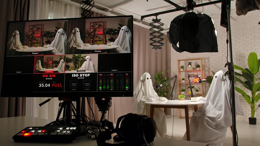 Backstage in the studio, a two people dressed as ghosts, wearing white sheets, record a podcast at a studio table with microphones. Perfect for Halloween, comedy, and entertainment.