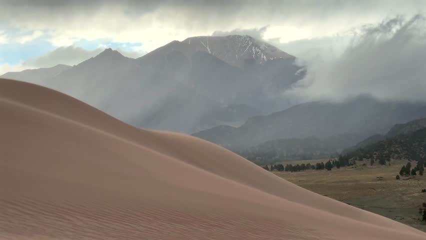 Stormy Great Sand Dunes National Park walking in windy sand sitting down Spring summer foggy cloudy raining mist Crestone Needle peak Colorado Sangre de Cristo range Rocky Mountains hills windy