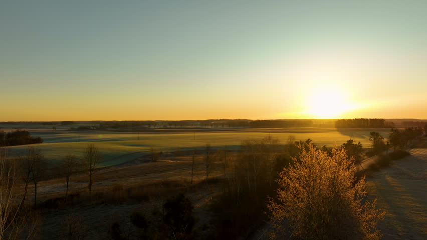 Golden sunrise over frosty rural fields with winter landscape and morning light.