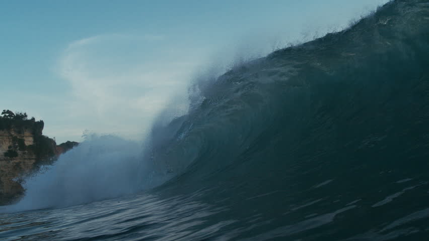 Large wave crashes near rocky point in tropical setting with vibrant slow textured motion