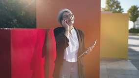 Confident mature businesswoman holding tablet and speaking on mobile phone outdoors, representing communication, leadership, and digital connection in modern professional life - Powered by Shutterstock - Get 15% off with code: PIKWIZARD15