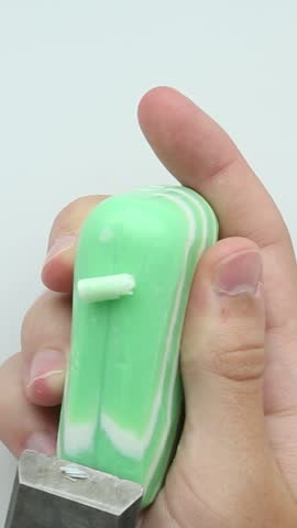 Hands hold a green soap bar while a blade slices through it, creating satisfying chunks and shavings during relaxing soap cutting ASMR session