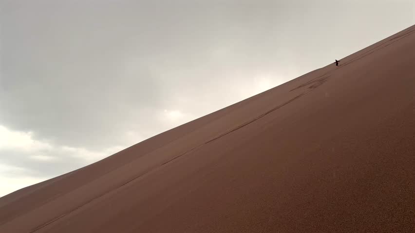Person running down the Great Sand Dunes National Park Sangre de Cristo range Rocky Mountains spring summer raining cloudy Colorado unique magical large amounts of sand dune hills windy landscape