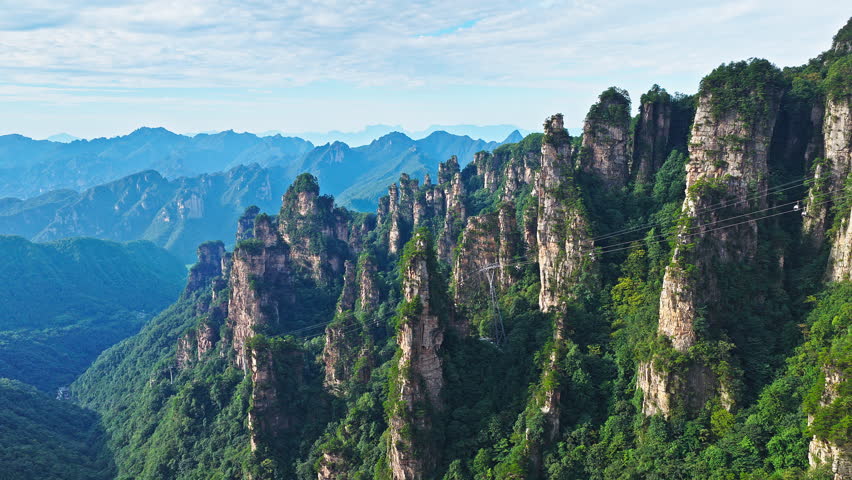 Aerial shot of the spectacular mountain landscape with unique rock pillars, lush green forest, and a cable car. Famous Zhangjiajie national forest park  in Hunan, China.