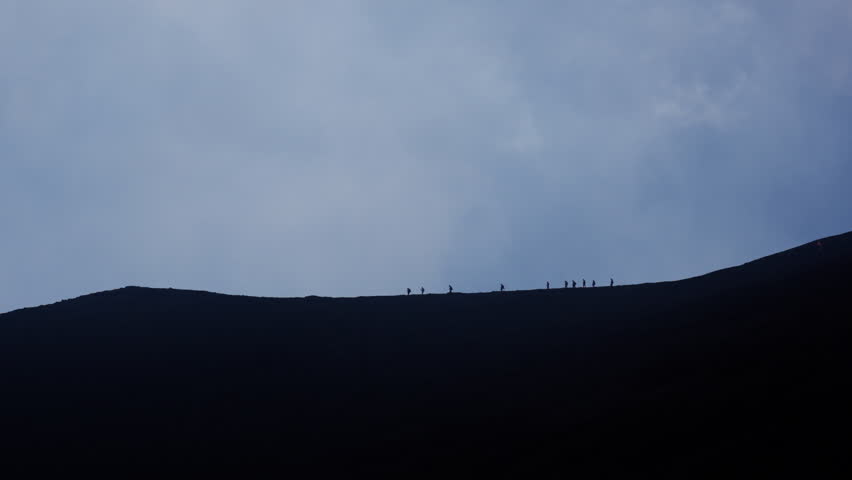Silhouettes trekking on Mount Etna, conveying adventure against sky