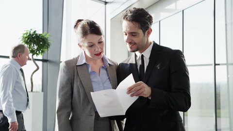 An attractive young businessman and businesswoman meet to discuss a business contract in the lobby of a light and contemporary office building.
