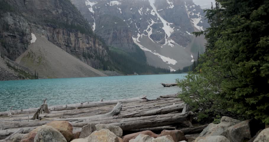 Moraine lake on a foggy and rainy day with beautiful blue water and glacier covered mountains in the background.