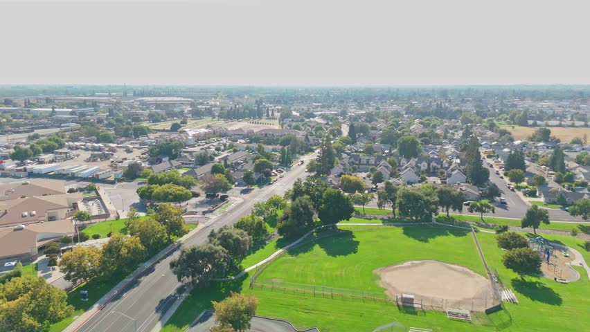 Drone zoom in of Sierra View neighborhoods in Oakdale, California with rooftops, suburban streets, and surrounding open land, perfect for community, housing, and real estate stock video.