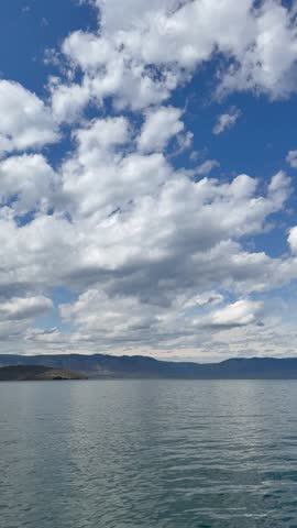 Lake Baikal on a sunny day. Vertical video of the Small Sea and the shores of Olkhon Island from a ferry. Beautiful blue sky with cumulus clouds over blue water. Natural background. Scenic skyscape