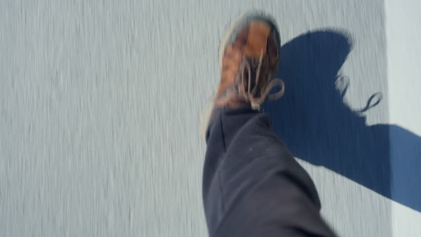 Handheld POV of a man’s feet walking forward on asphalt, capturing natural motion and urban texture from above.