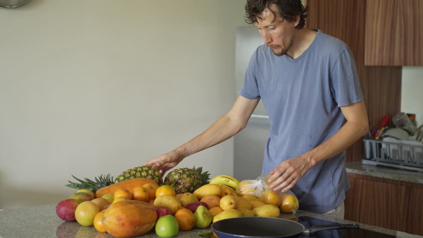 A young man places fresh fruits on a table in a kitchen, preparing a healthy and colorful arrangement. A moment of homemaking, wellness, and mindful living in a bright and inviting space.