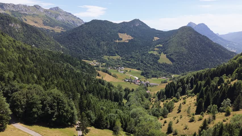 Cinematic drone orbital shot circling a traditional alpine village in the Bauges Massif, French Alps. Scenic rural landscape with mountains, meadows, and authentic French countryside.