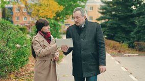 Man woman business people with digital tablets walking talking outdoors in autumn. Woman man working with tablet computer in hands. Business people working in autumn park. Companions walking outdoors - Powered by Shutterstock - Get 15% off with code: PIKWIZARD15