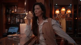 Woman drinking whiskey from glass at bar, relaxing in evening. Bar counter with snacks and drinks in background. Indoor setting with dim lighting and cozy ambiance, enjoying leisure time - Powered by Shutterstock - Get 15% off with code: PIKWIZARD15