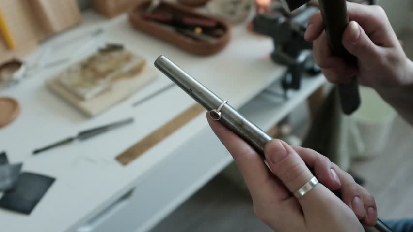 Closeup of a skilled female jeweler hammers a ring into shape. Small business craftsmanship in a bright modern workshop. The detailed process of traditional jewelry making. Artisan woman.