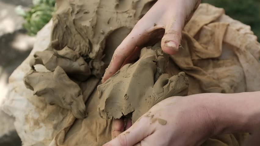 Closeup horizontal video of working with wet clay. Hands separate small lumps of clay, kneading the clay for handmade craft pottery.