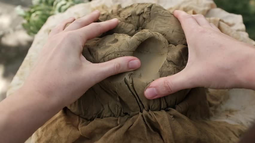 Closeup horizontal video of working with wet clay. Hands separate small lumps of clay, kneading the clay for handmade craft pottery.