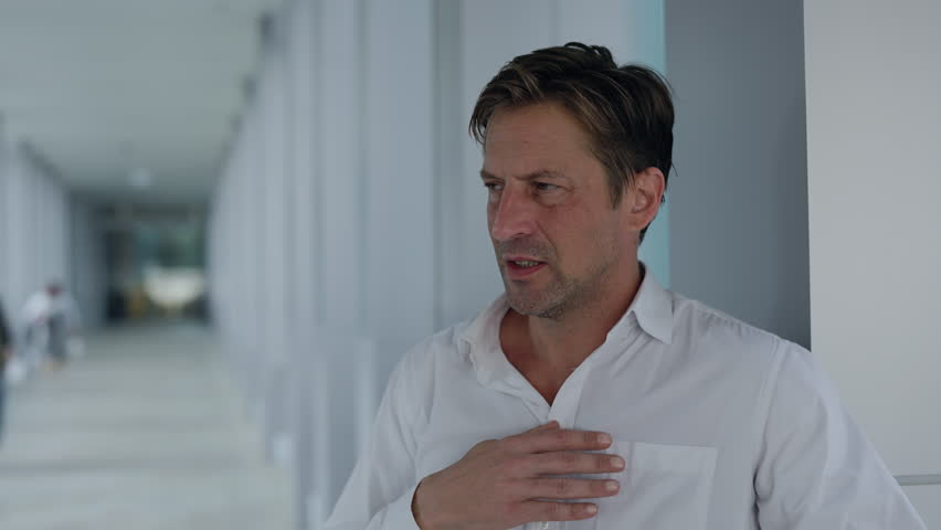 Portrait of businessman feels strong pain and massages chest in office lobby. Mature man corporate manager deals with heart attack symptoms near metal railing in business center