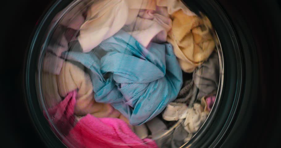 Colorful wet clothes spinning inside washing machine drum, creating mesmerizing circular motion and revealing rhythmic domestic cleaning process. Washing colored clothes in washing machine