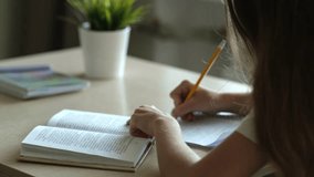 Teen girl student writing in notebook with pencil sitting at table. Child doing homework, studying at home. Education and school tasks concept - Powered by Shutterstock - Get 15% off with code: PIKWIZARD15