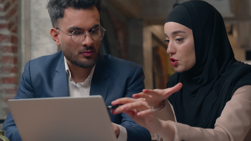 Muslim business team two managers man woman looking laptop discuss project startup brainstorming Islamic businesswoman in hijab Indian businessman working together communicate negotiate in office - Powered by Shutterstock - Get 15% off with code: PIKWIZARD15