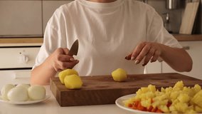 Close-up of a woman expertly cutting fresh potatoes on a wooden cutting board in a warm kitchen. A plate of diced vegetables and boiled eggs adds to the meal prep atmosphere - Powered by Shutterstock - Get 15% off with code: PIKWIZARD15